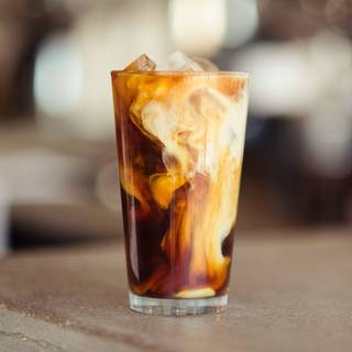 glass of ice coffee with milk mixing in