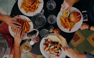 overview shot of table with people's hands over plate of burgers and fries