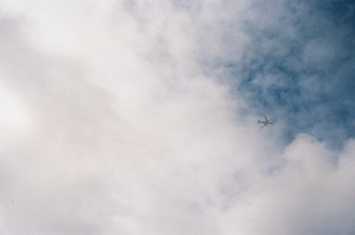 Picture of an airplane flying high above the city with wide open blue sky