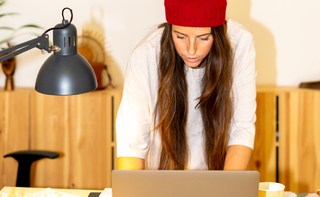 A woman in a red beanie working on her laptop computer using wi-fi